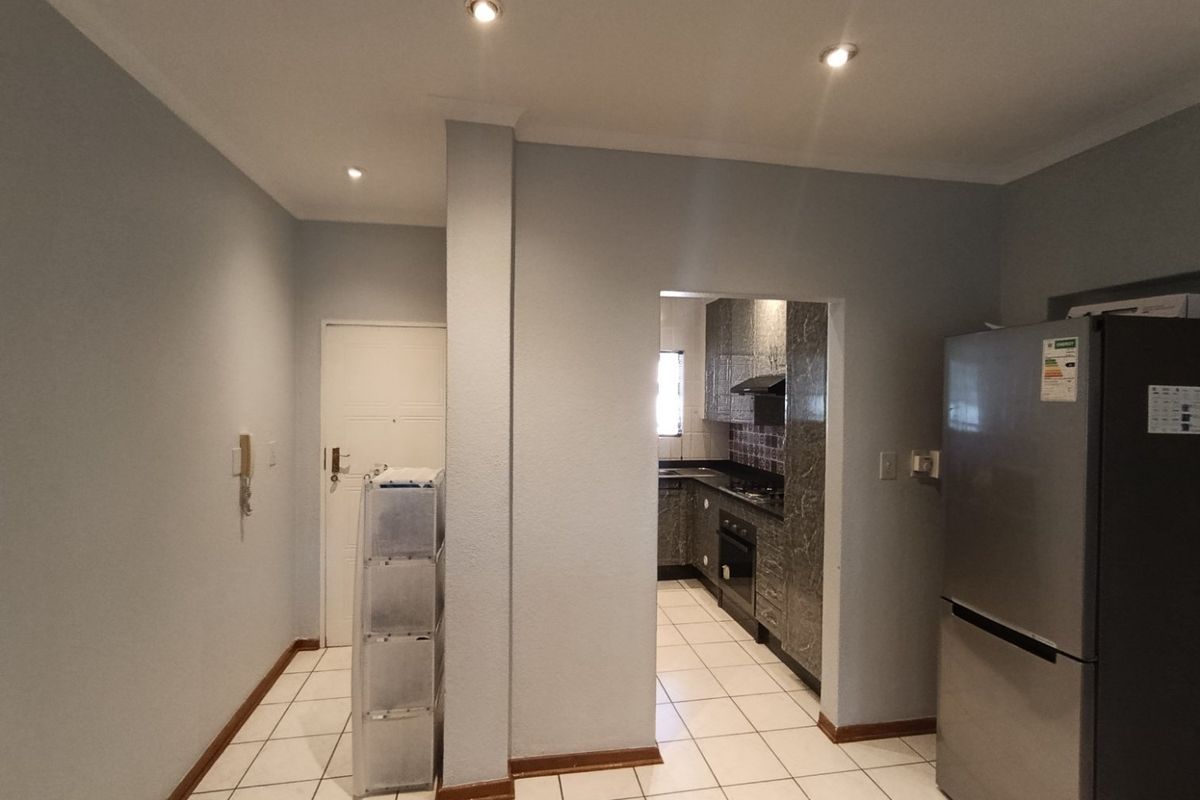 A functional kitchen area featuring tiled flooring, built-in cabinetry, and integrated appliances, with an adjacent entryway and intercom system.