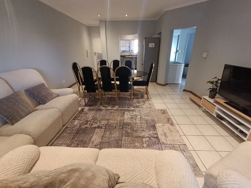 An open-plan living and dining area featuring neutral wall tones, ceramic floor tiles, and recessed downlighting, providing a functional and connected living space.