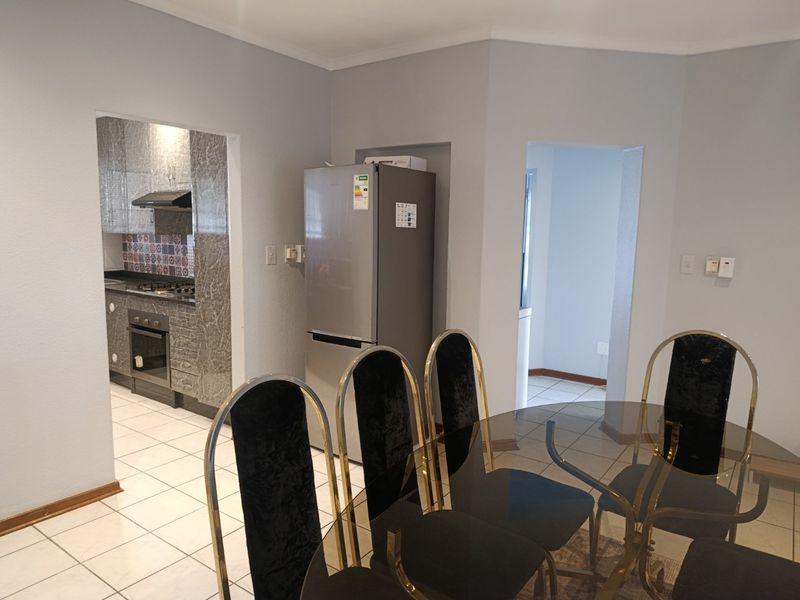 Open plan dining area adjacent to a compact kitchen featuring tiled floors, built-in oven, gas hob, and decorative backsplash tiling.