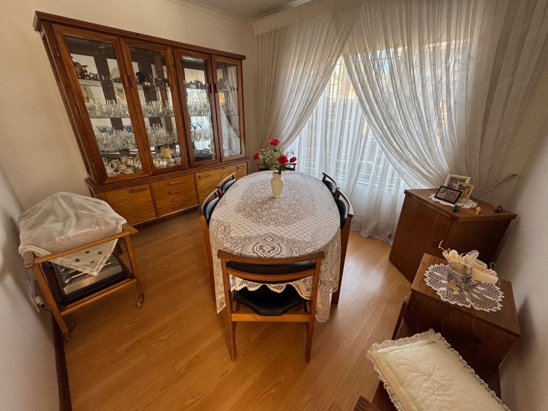 A dining room featuring laminate flooring and large windows with sheer curtains, providing a functional space for meals.