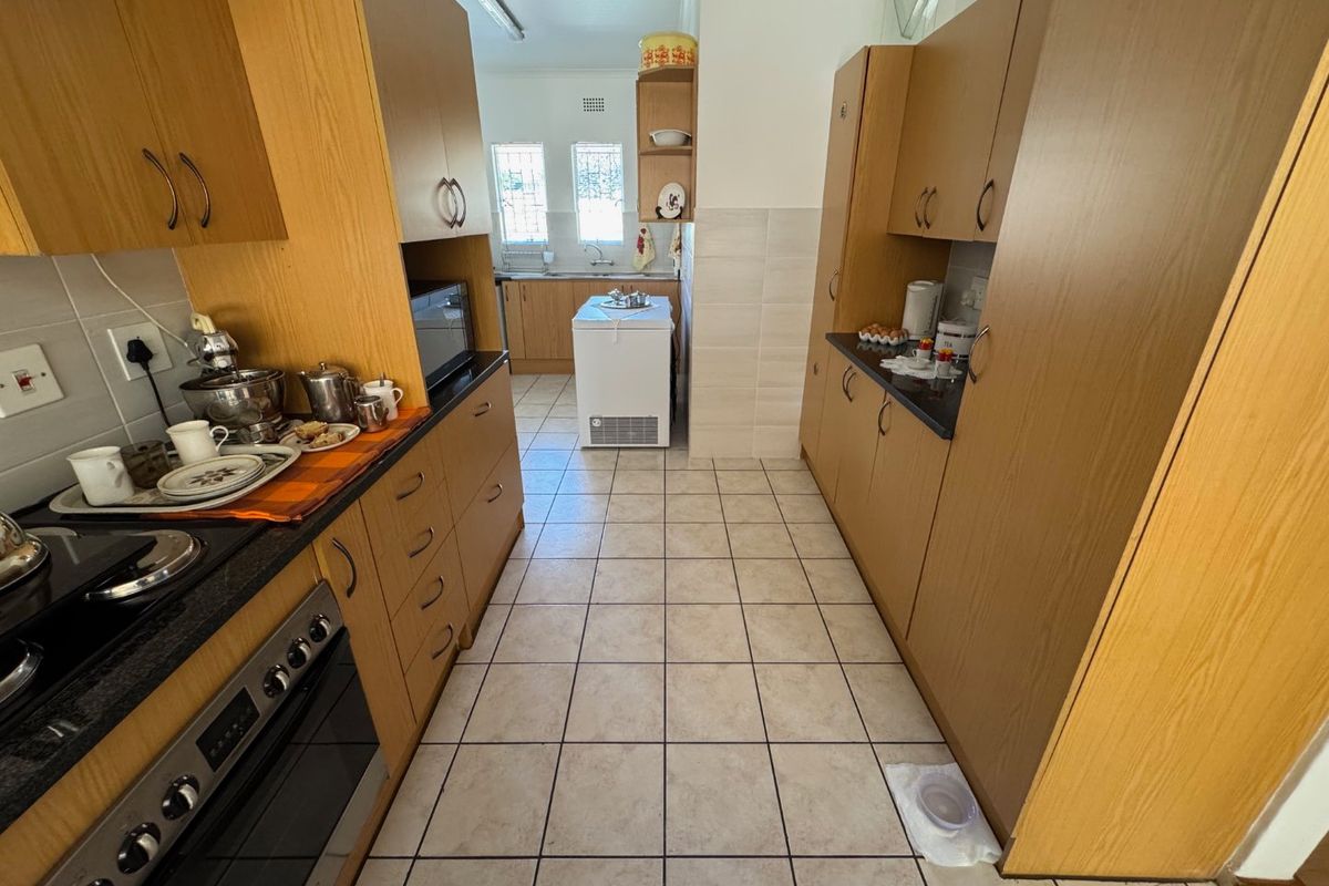 A functional galley-style kitchen featuring wood-look cabinetry, dark countertops, built-in oven, and tiled flooring with a separate prep area.