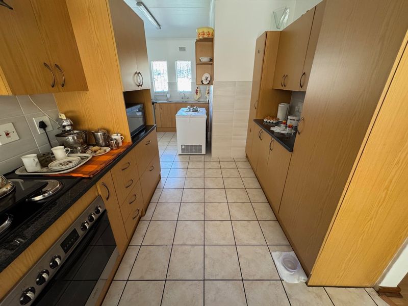 A functional galley-style kitchen featuring wood-look cabinetry, dark countertops, built-in oven, and tiled flooring with a separate prep area.