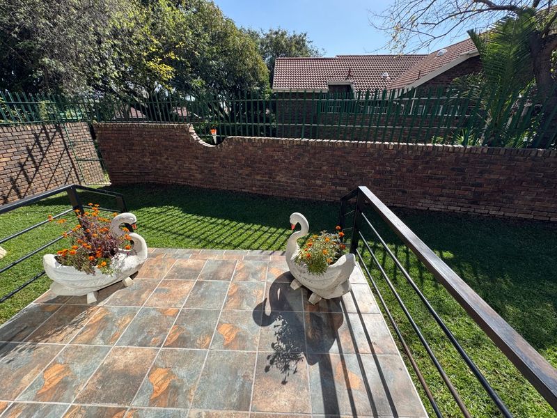 A private tiled patio area overlooking a small garden, enclosed by a brick boundary wall and metal security fencing.