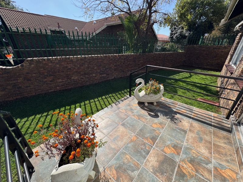 A private tiled patio area featuring metal railings and a brick boundary wall, overlooking a small garden space.