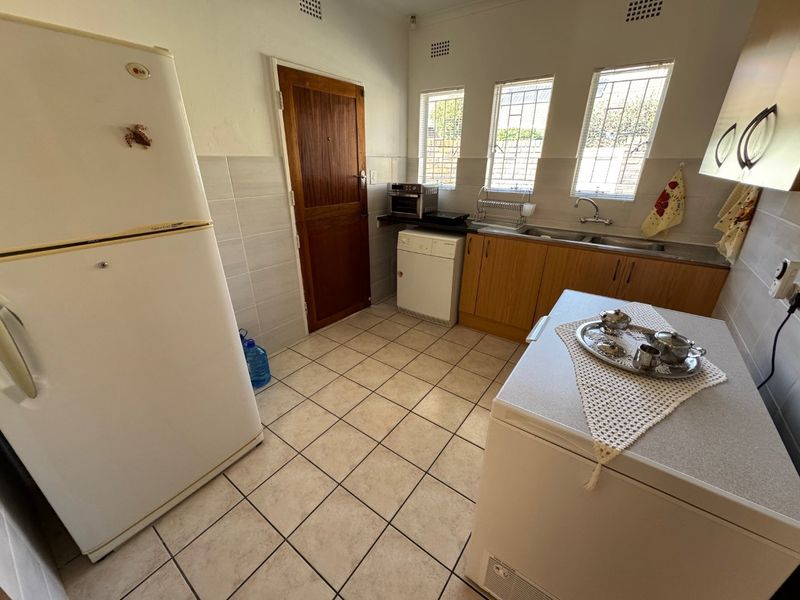 A functional kitchen featuring laminate cabinetry, tiled flooring, and a stainless steel sink, with security bars installed on the windows.