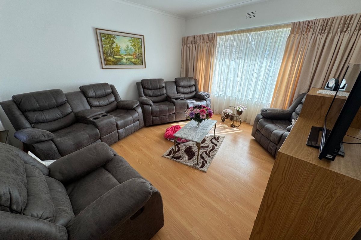 A comfortable living room featuring laminate flooring and large windows with curtain treatments, providing a functional and well-lit space for relaxation.