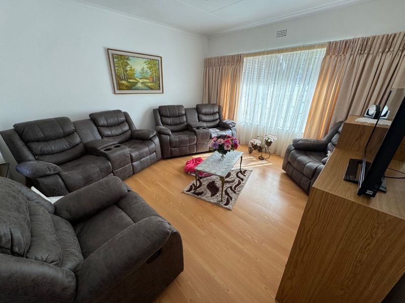 A comfortable living room featuring laminate flooring and large windows with curtain treatments, providing a functional and well-lit space for relaxation.