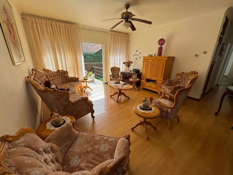 A well-maintained living room featuring laminate flooring, a ceiling fan, and direct access to an outdoor patio area through a sliding glass door.