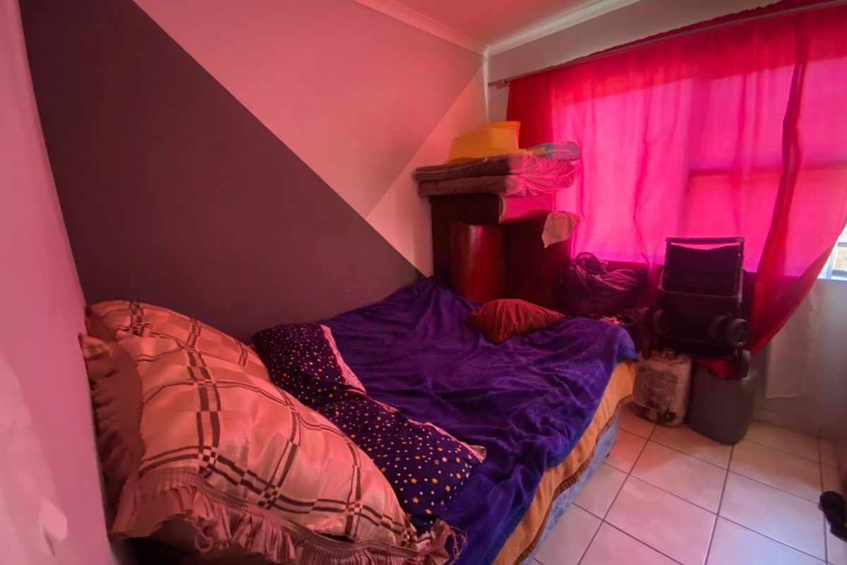 A bedroom featuring tiled flooring and a two-tone painted wall, currently used as a sleeping area.