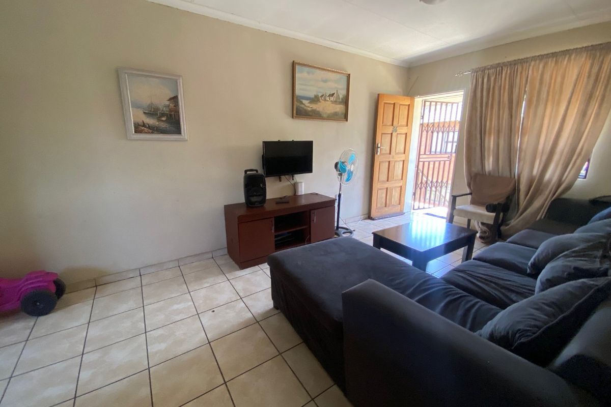 A living room featuring tiled flooring, a timber entrance door with a security gate, and standard ceiling lighting.