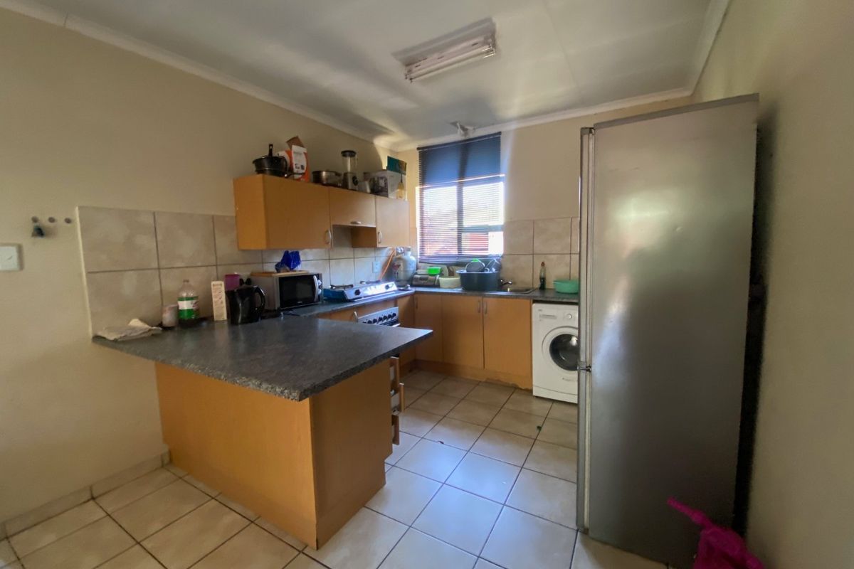 A functional kitchen featuring laminate cabinetry, tiled backsplash, tiled flooring, and integrated laundry plumbing, offering potential for modernization.