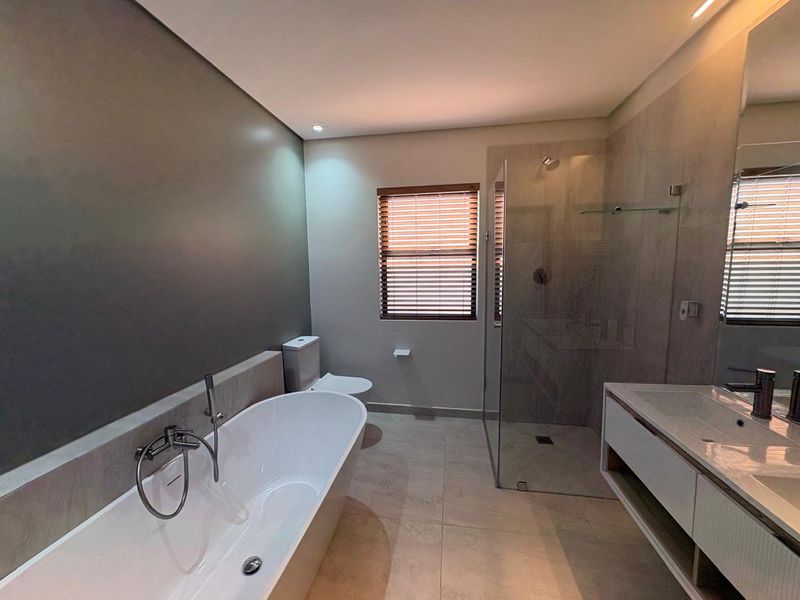 Modern bathroom featuring a sleek freestanding bathtub, a spacious walk-in shower with glass enclosure, and a contemporary wall-mounted vanity unit.