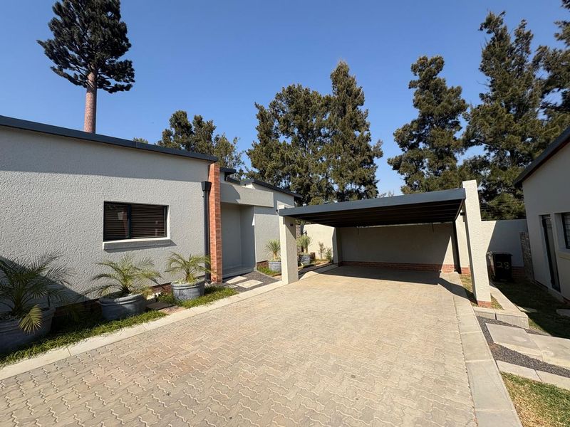 Front exterior view of the townhouse featuring a paved driveway, a modern carport, and well-maintained stucco facade with brick detailing.