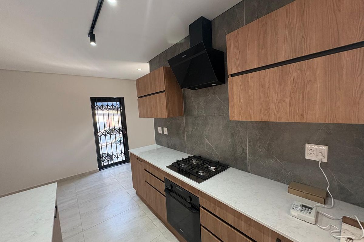 Modern kitchen featuring wood-finish cabinetry, stone countertops, built-in gas hob, oven, extractor fan, and stylish dark tiled splashback.