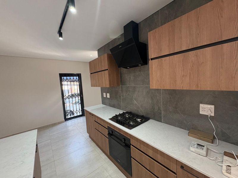 Modern kitchen featuring wood-finish cabinetry, stone countertops, built-in gas hob, oven, extractor fan, and stylish dark tiled splashback.
