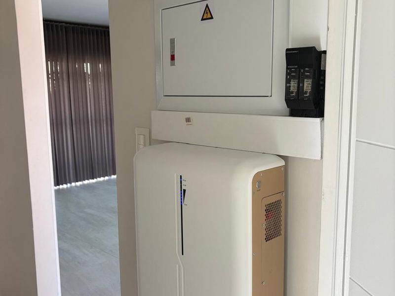 A clean utility area featuring a modern wall-mounted solar inverter and electrical distribution board.