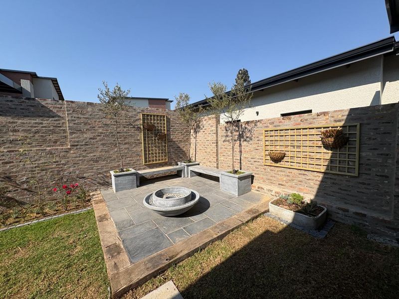 A well-maintained rear courtyard featuring a stone-paved patio, built-in concrete benches, integrated planters, and decorative timber trellises against a brick boundary wall.