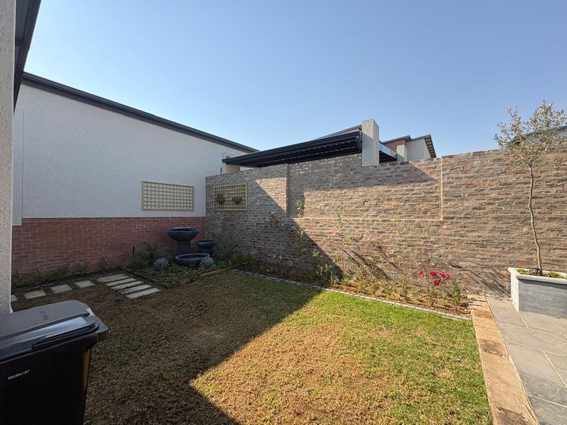 A well-maintained rear garden featuring a brick boundary wall, a small lawn, and a paved patio area with a pergola structure.