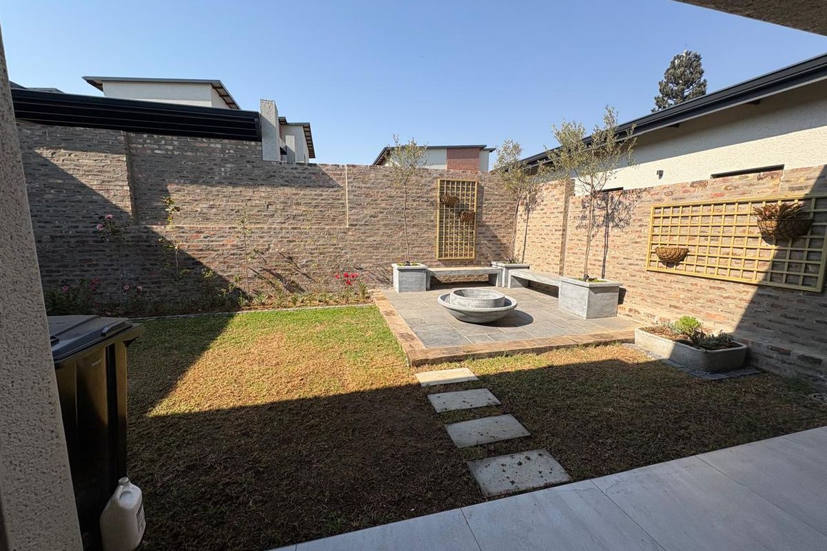 A private rear courtyard featuring a brick-walled garden, stone-paved patio area with a built-in concrete bench, fire pit, and manicured lawn.