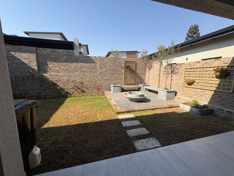 A private rear courtyard featuring a brick-walled garden, stone-paved patio area with a built-in concrete bench, fire pit, and manicured lawn.