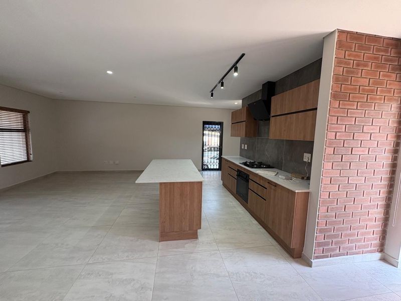 Modern open-plan kitchen and living area featuring a central island, built-in appliances, sleek cabinetry, and a striking exposed brick feature wall.