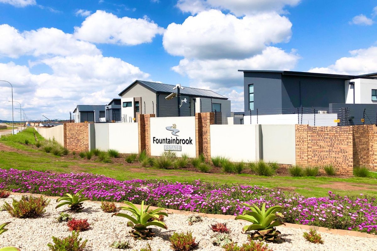 Entrance view of Fountainbrook Estate featuring a modern brick boundary wall, electric fencing, security infrastructure, and well-maintained landscaped gardens.