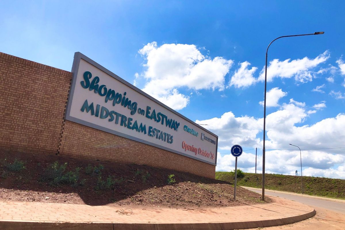 A street-level view of a brick boundary wall featuring signage for a local shopping center development in Midstream Estates.