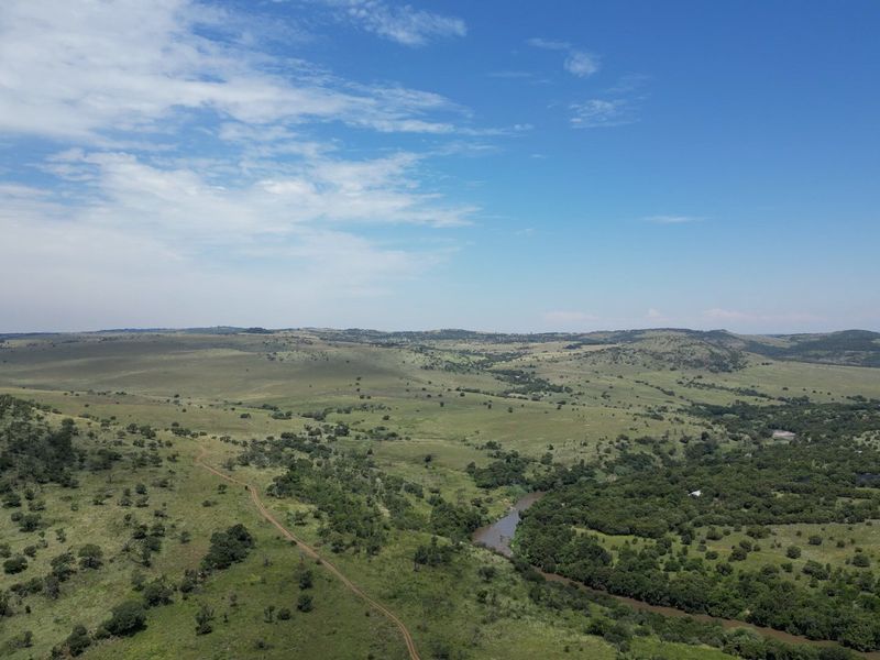 An expansive aerial view of the farm property featuring rolling hills, natural vegetation, and a winding river.