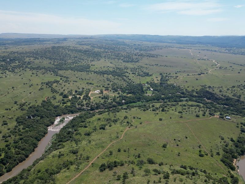 An expansive aerial view of the farm property, showcasing the natural landscape, winding river, and surrounding rural terrain.