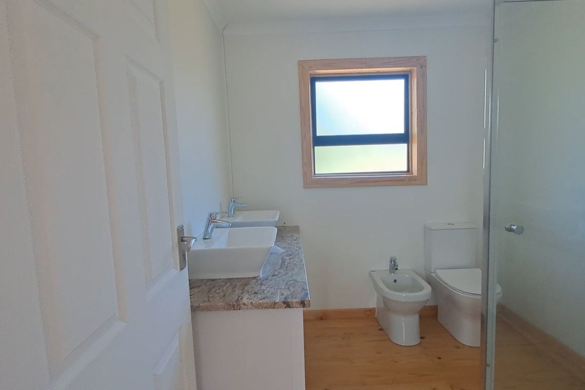 A clean, modern bathroom featuring a double vanity with vessel sinks, granite countertop, bidet, toilet, and a glass-enclosed shower with timber flooring.