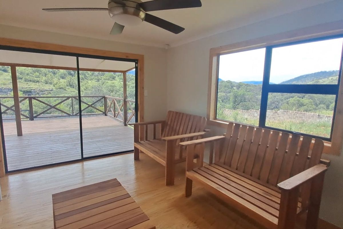 Bright living area featuring timber flooring, ceiling fan, and large windows with direct access to an expansive outdoor wooden deck with scenic views.