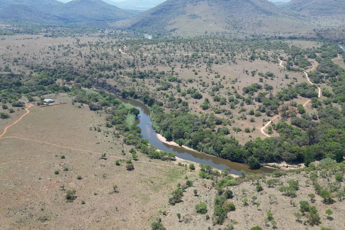 An aerial view of the expansive farm property featuring a winding river, natural vegetation, dirt access roads, and a fenced enclosure.