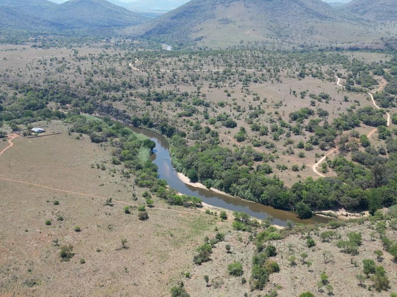 An aerial view of the expansive farm property featuring a winding river, natural vegetation, dirt access roads, and a fenced enclosure.