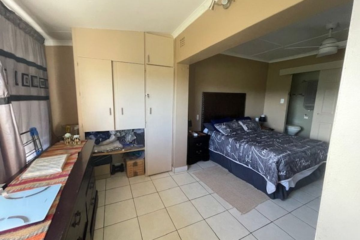 Bedroom featuring built-in cupboards, ceramic floor tiles, and an en-suite bathroom access point. The space requires cosmetic updates to improve its overall condition.