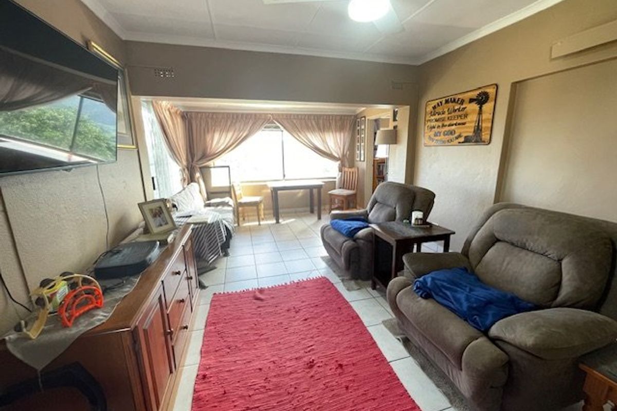 A living room featuring tiled flooring, a ceiling fan, and large windows that provide natural light to the space.