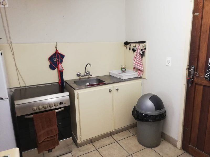 A compact kitchen area featuring a stainless steel sink, built-in cabinetry, and a freestanding stove with tiled flooring.