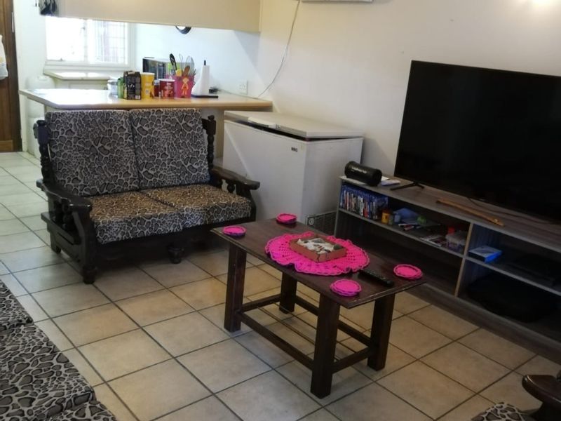 Open-plan living area featuring ceramic floor tiles, a breakfast bar connecting to the kitchen, and a wall-mounted air conditioning unit.