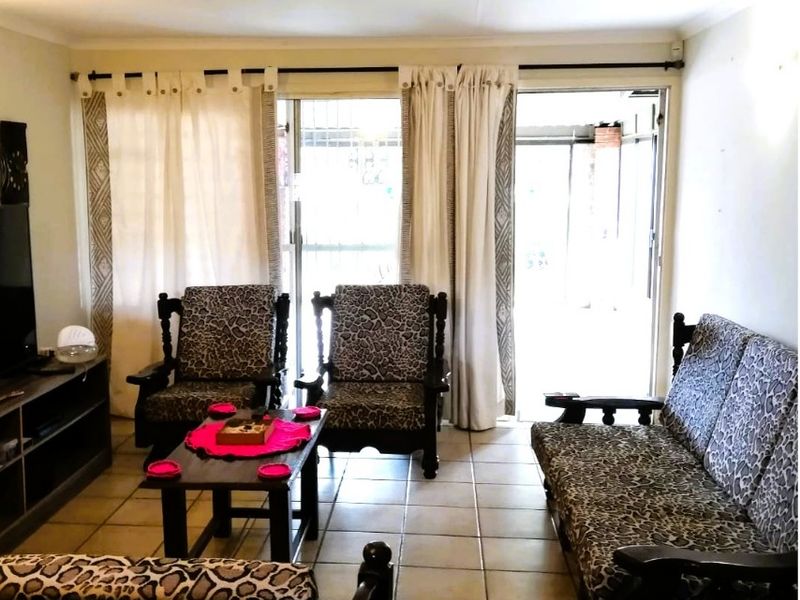 A living room featuring tiled flooring and a sliding glass door with an integrated security gate, providing access to the exterior.