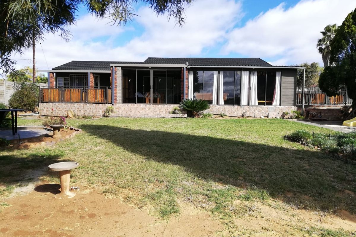 Rear view of the house featuring a spacious lawn, a tiled patio area, and large sliding glass doors providing seamless indoor-outdoor flow.