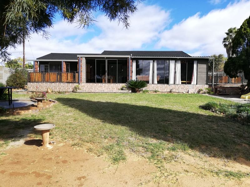 Rear view of the house featuring a spacious lawn, a tiled patio area, and large sliding glass doors providing seamless indoor-outdoor flow.