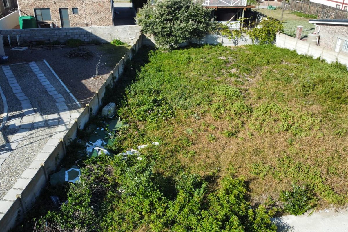 Aerial view of a vacant residential plot featuring boundary walls and an existing paved driveway area, currently requiring clearing of vegetation and debris.