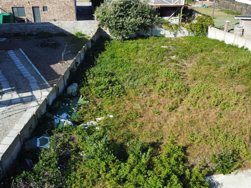 Aerial view of a vacant residential plot featuring boundary walls and an existing paved driveway area, currently requiring clearing of vegetation and debris.