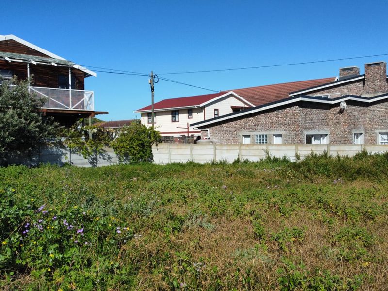 A vacant residential plot featuring natural vegetation, enclosed by a precast concrete boundary wall with surrounding residential properties visible in the background.