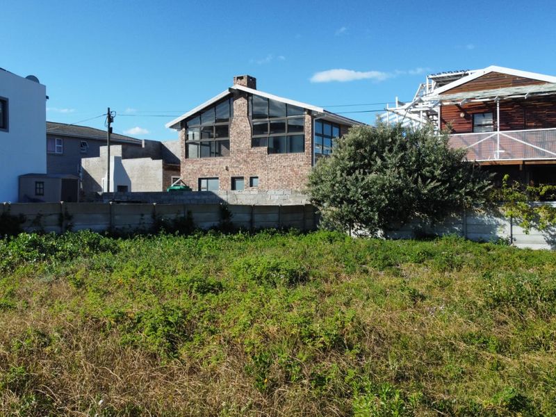 A vacant residential plot featuring a precast concrete boundary wall and overgrown vegetation, situated in a developed neighborhood.