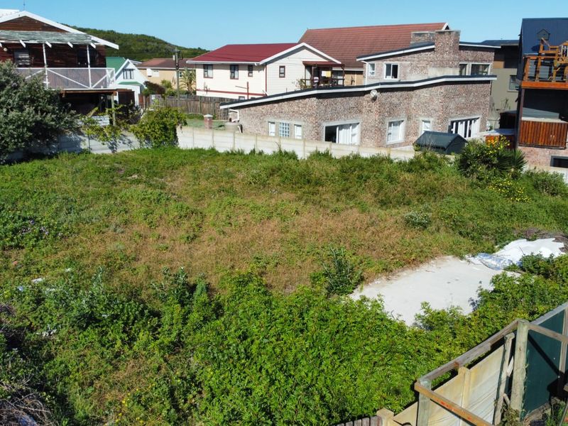 An elevated view of a vacant residential plot featuring overgrown vegetation, a concrete slab, and surrounding boundary walls in a developed neighborhood.
