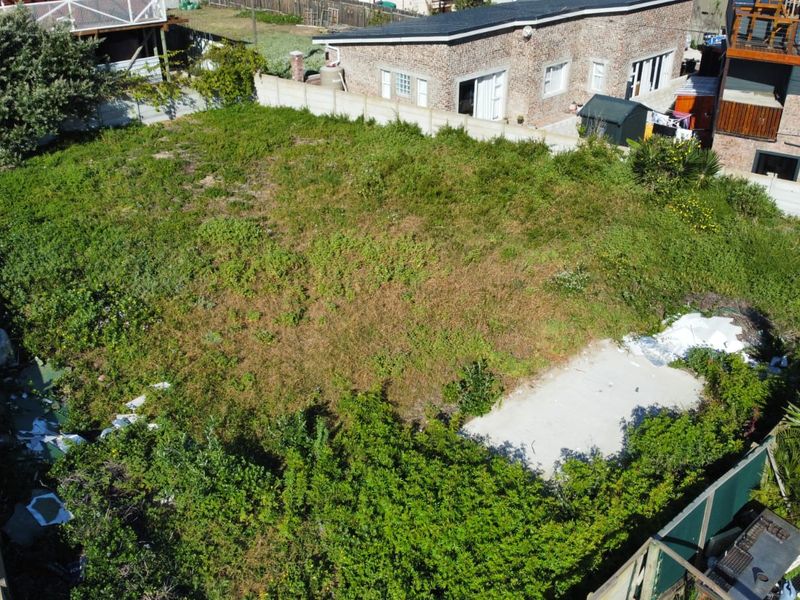 Aerial view of a vacant residential plot featuring overgrown vegetation and a concrete slab foundation, enclosed by boundary walls.