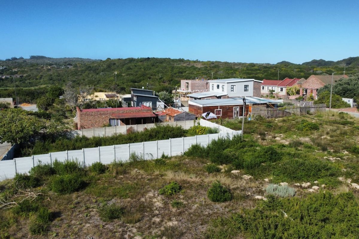 Aerial view of a vacant residential plot featuring natural vegetation and a precast concrete boundary wall in a developed neighborhood.