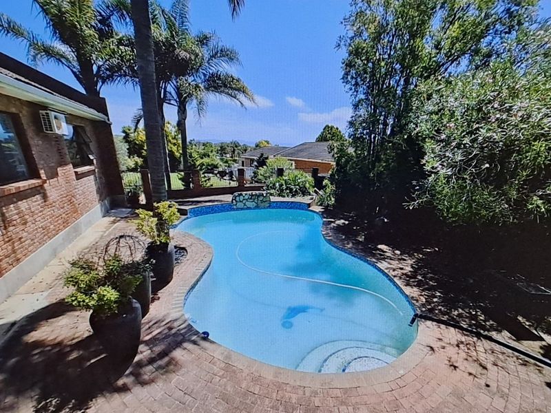 Outdoor pool area featuring a kidney-shaped swimming pool surrounded by brick paving and established garden landscaping.