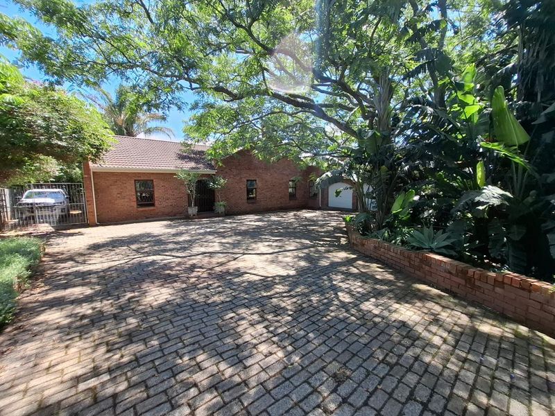 Front view of a brick house featuring a paved driveway, mature trees, and a secure garage entrance.