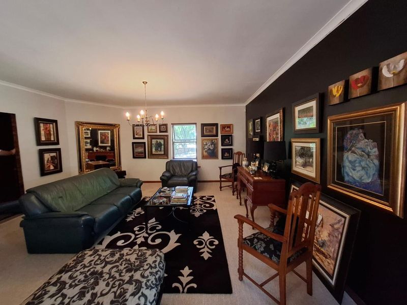 A spacious living room featuring a dark accent wall, neutral carpeting, and a classic chandelier, offering a comfortable and well-defined seating area.